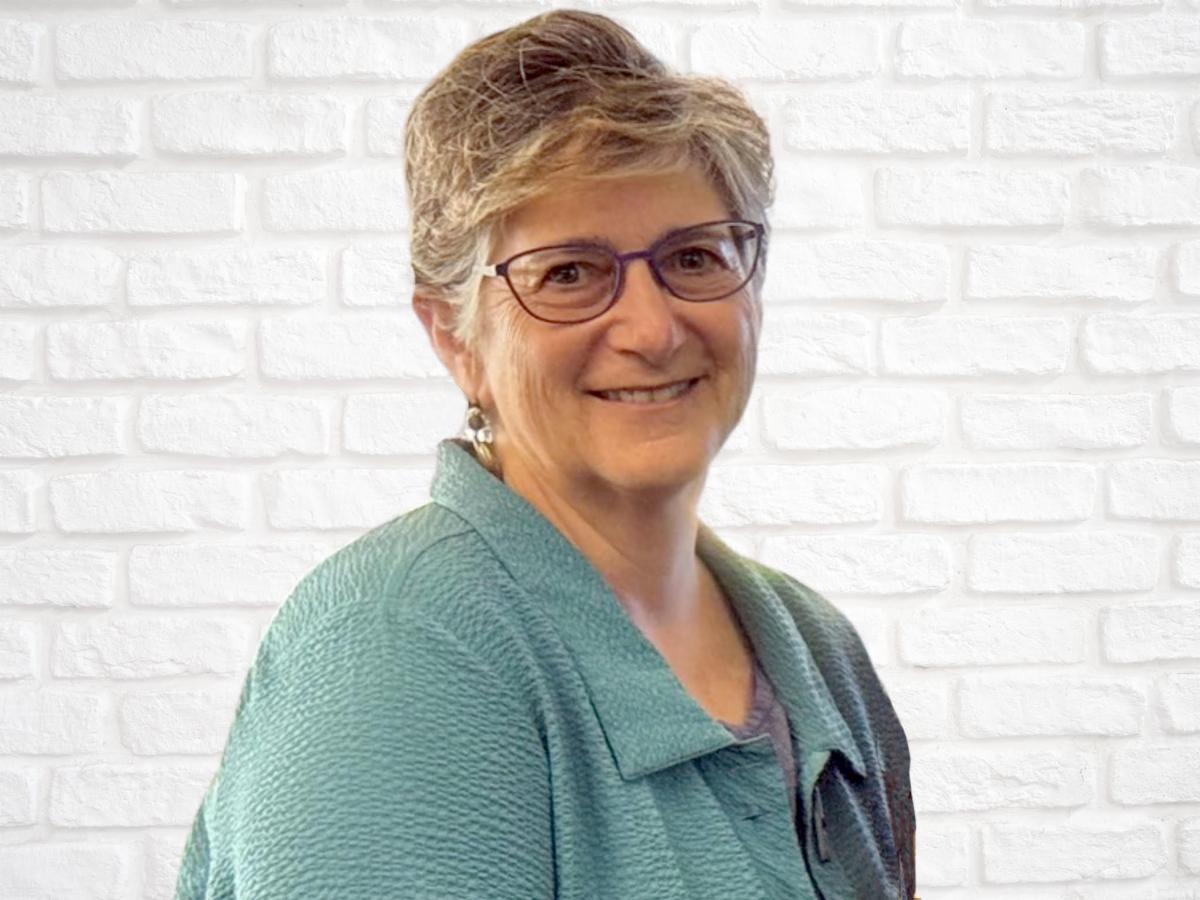 Headshot: Jean Hamerman, Executive Director, smiling in front of a white brick wall