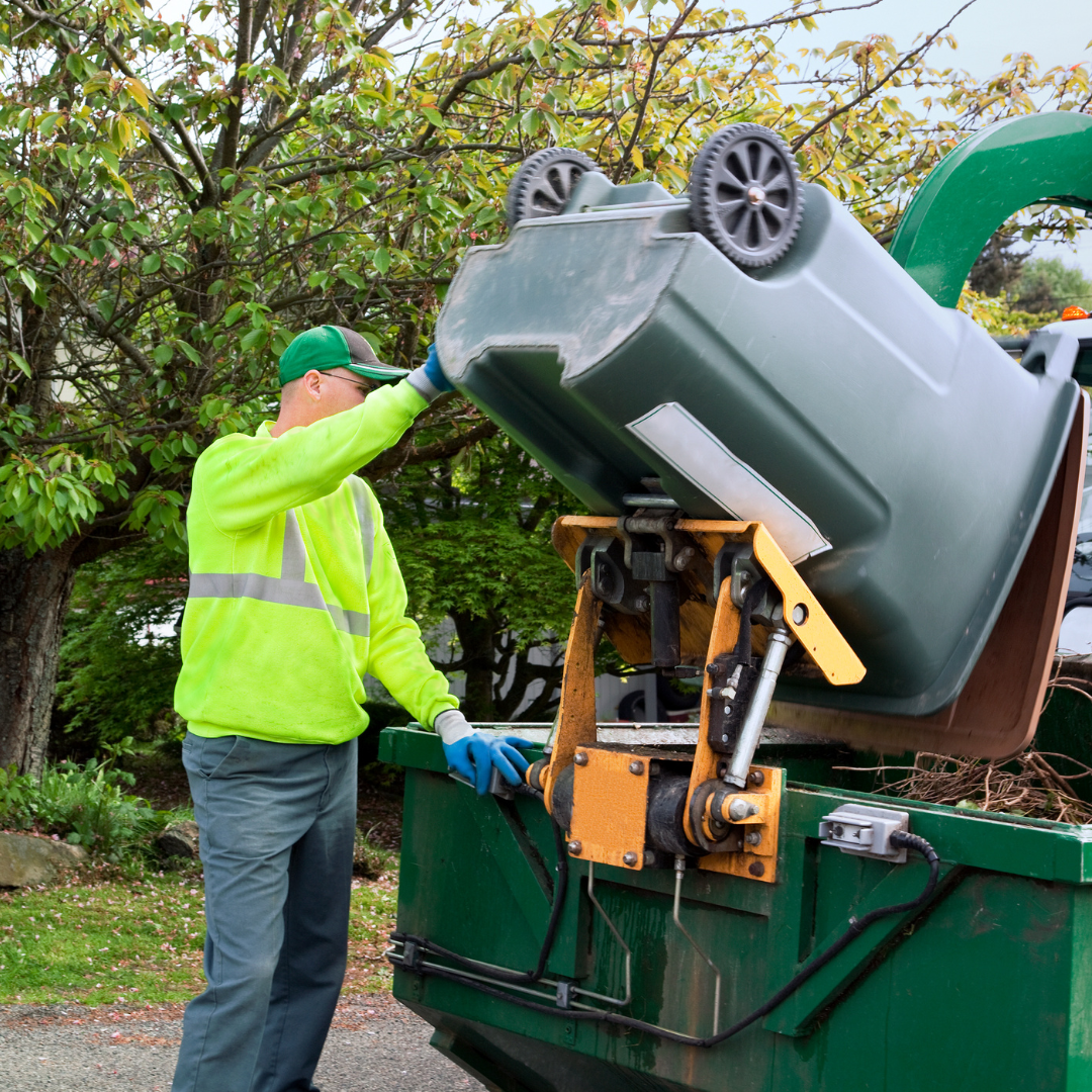 Person in a yellow work vest emptying a municipal trash bin into the back of a garbage truck