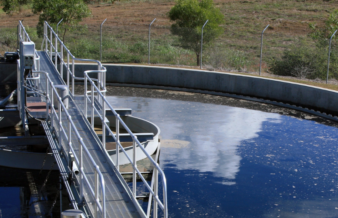Zoomed in image of an above ground water tank at a water treatment plant, tank and walkway visible with a fence and grass in the background