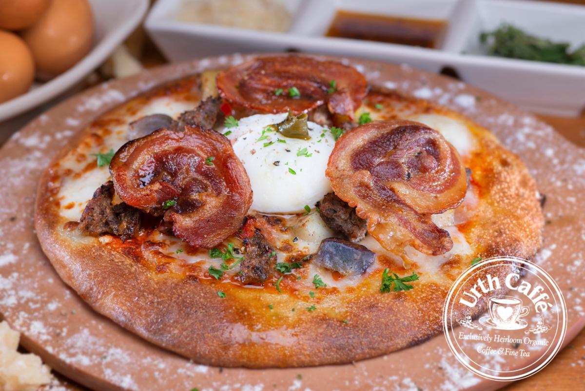 Photo of Urth Caffé Sunrise Pizza, on a cutting board with garnish. 