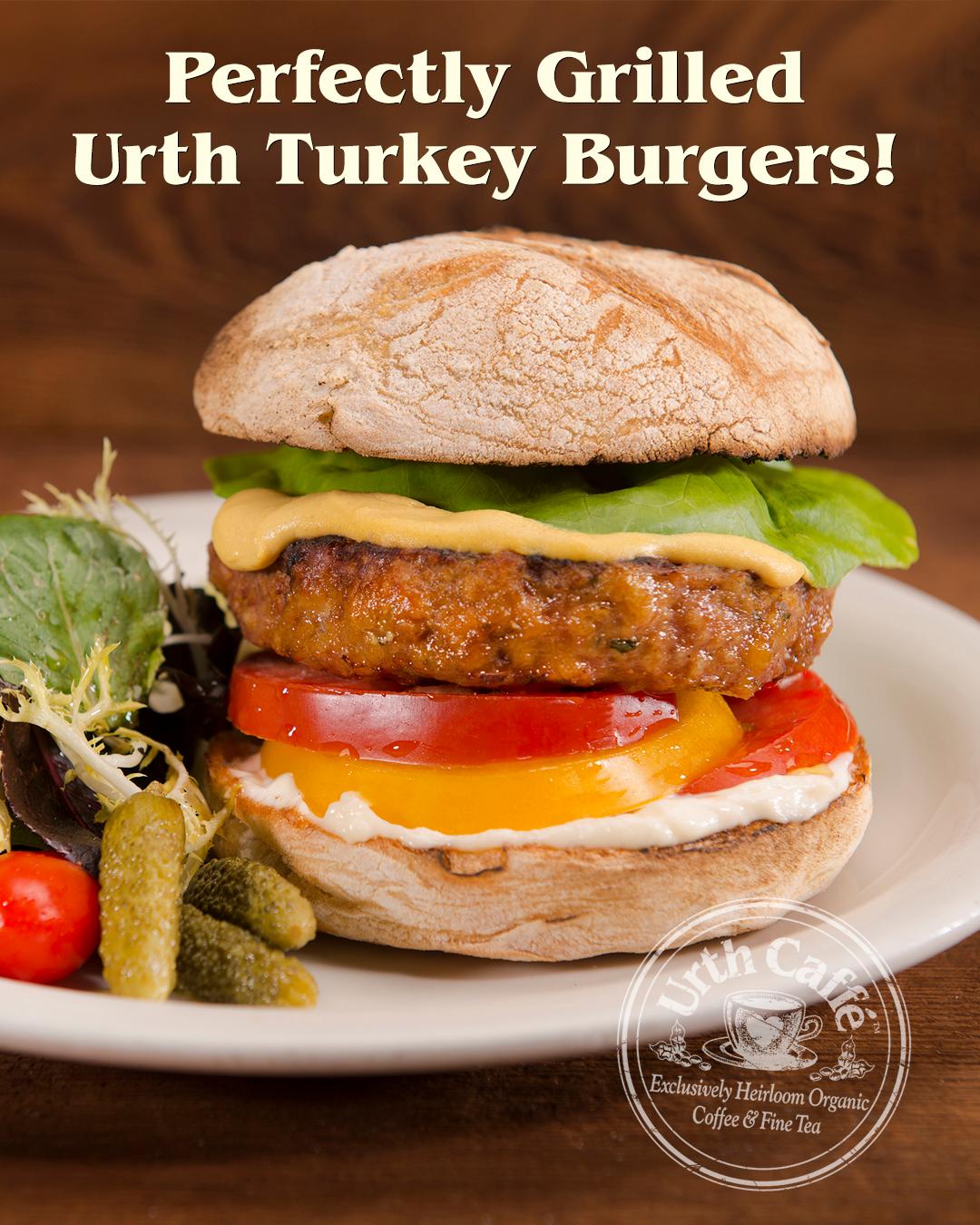 Photo of  Urth Caffé Turkey Burger, containing tomatoes, lettuce, mayonnaise, and mustard. To the left, a mixed greens salad with sprouts, pickles, and cherry red tomatoes on top.
