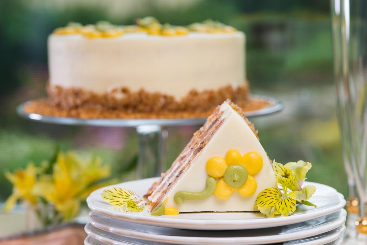 Urth Caffé Carrot cake slice on a plate with whole cake in the background.
