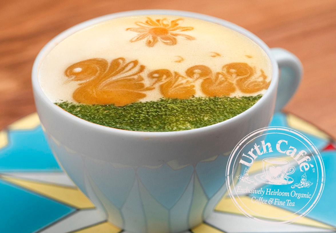 Photo of Urth Caffé Pistachio Latté, in a white ceramic cup on a wooden table, with decorative tile work on the bottom., with Urth logo and 