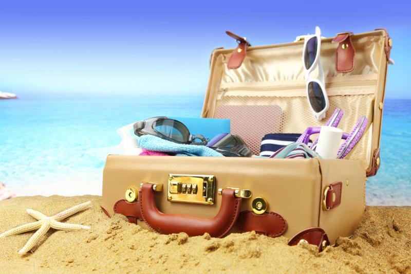 Full open suitcase on tropical beach background 