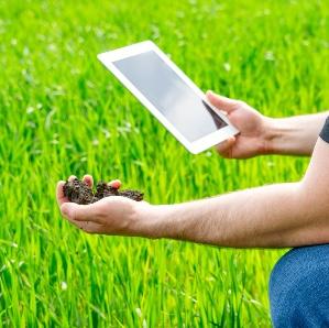A person in the lawn holding soil in their hand and a smart tablet in the other.