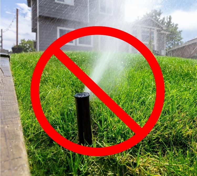 A lawn sprinkler in use with a red circle with a line through it.