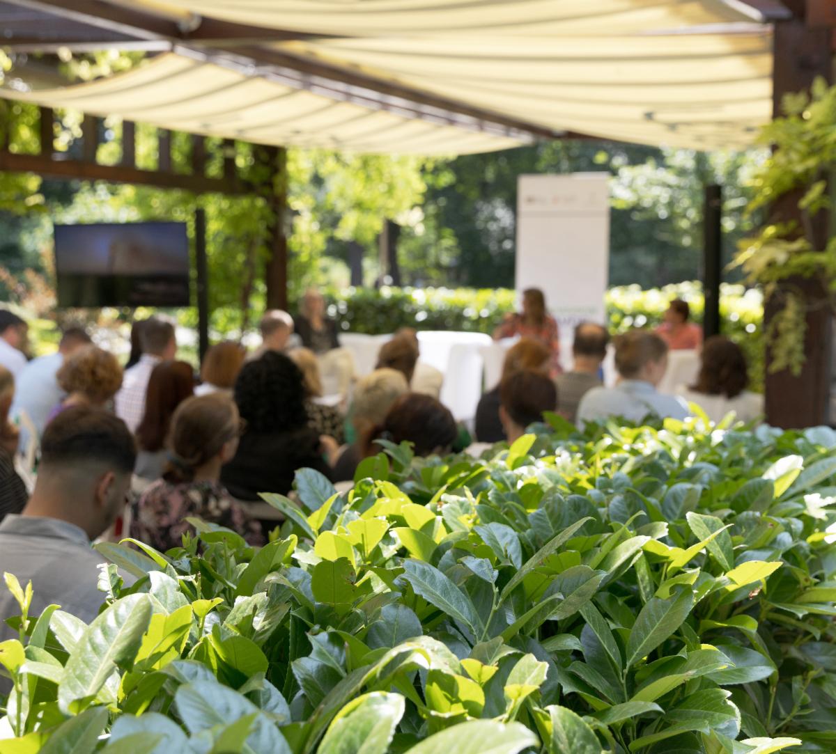 People attending an outdoor conference with plants in the foreground.