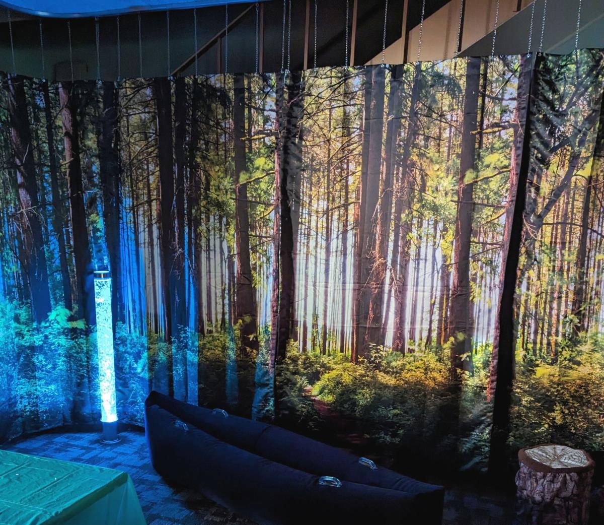 A bubble tube shows against forest-theme drapes with an inflatable blue canoe and a stump-like seat in the foreground.