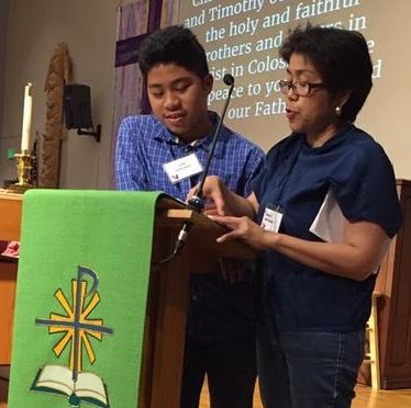 Youth stands behind lectern and reads scripture with his mom_s support. Both have brown skin and black hair reflecting their Filipino heritage