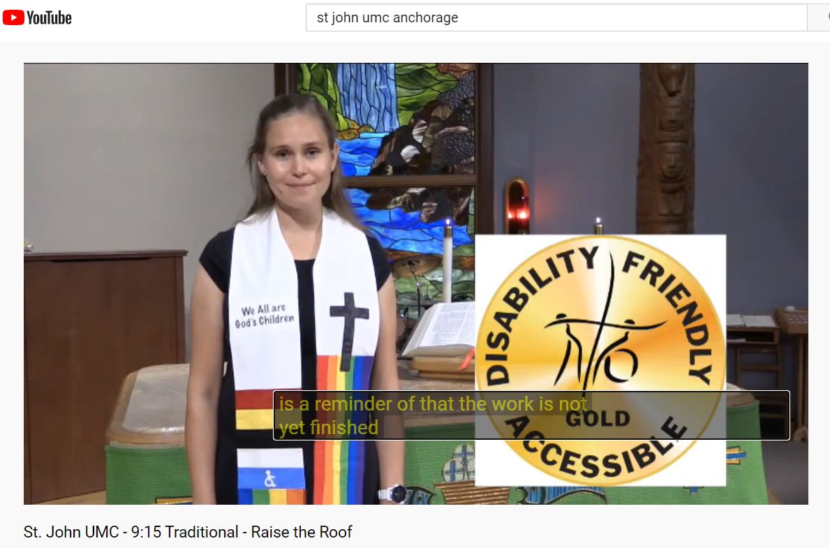 pastor_s whose stole includes access symbol stands in front of altar and stained glass with waterfall and eagle. Screen shot mage includes captioning and gold badge