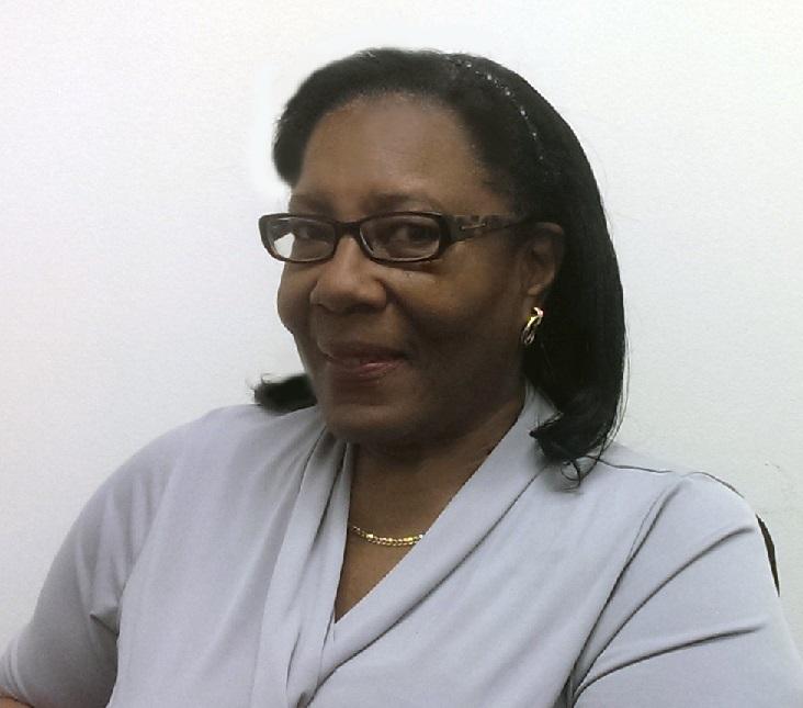 Woman with black hair and glasses wearing a grey top smiles at the camera. 