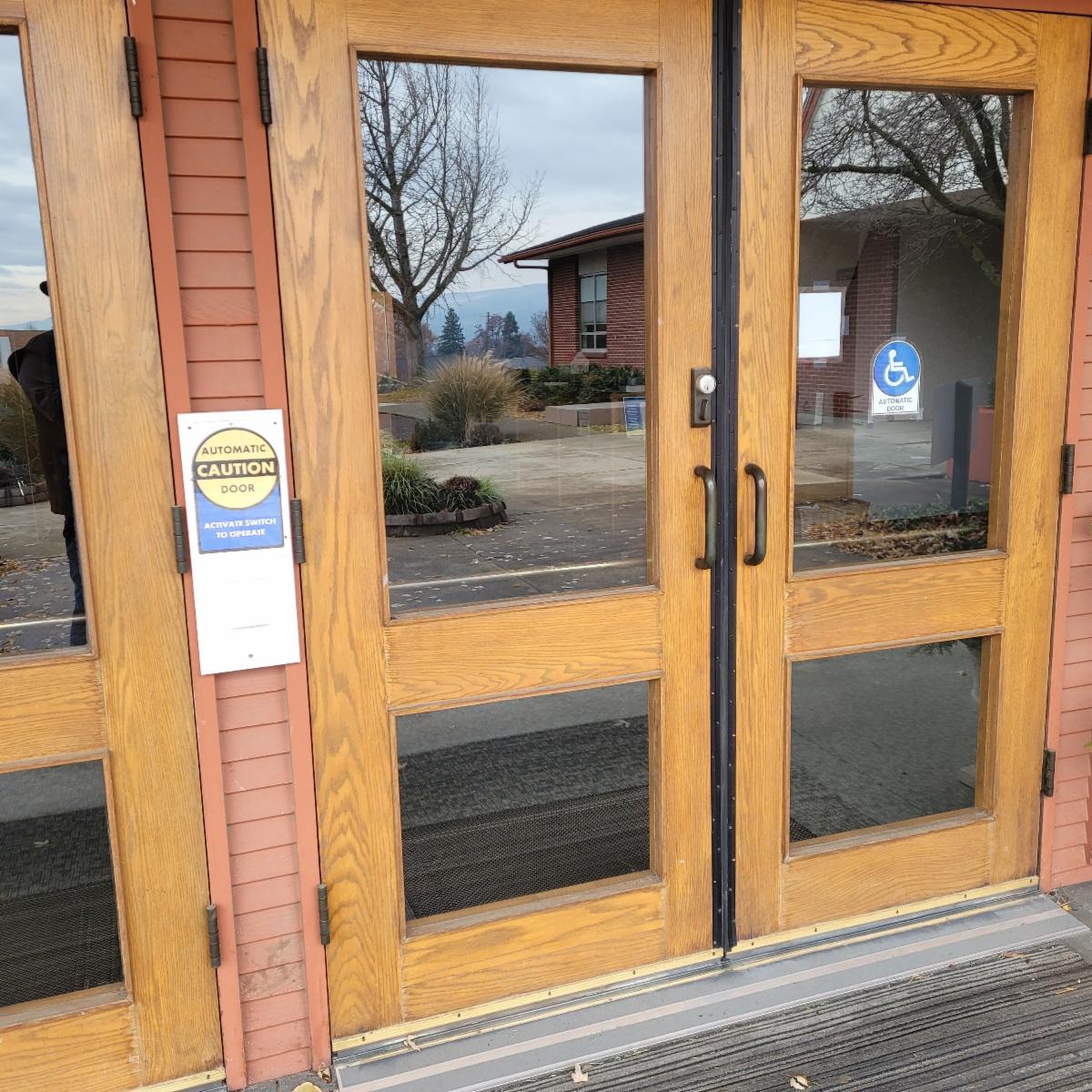A set of wooden and glass double entrance doors with decals indicating they are automatic doors.