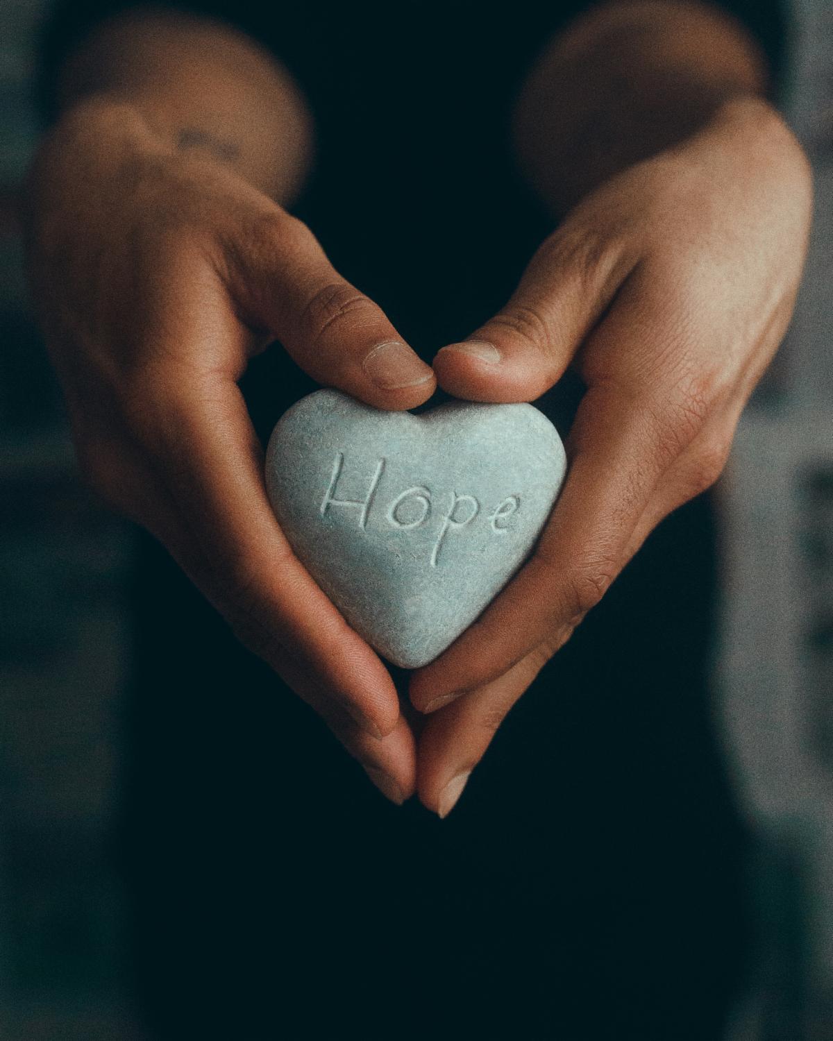 Two hands hold a heart-shaped rock with the word hope on it