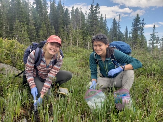 Two people wearing backpacks kneel in a field to take samples
