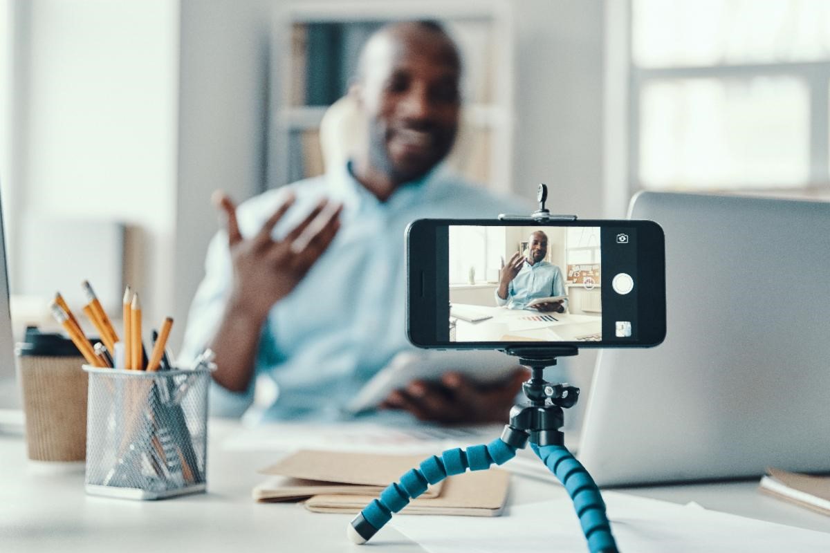 Photo a man sitting at his desk with his cellphone in a holding device recording a video of himself speaking