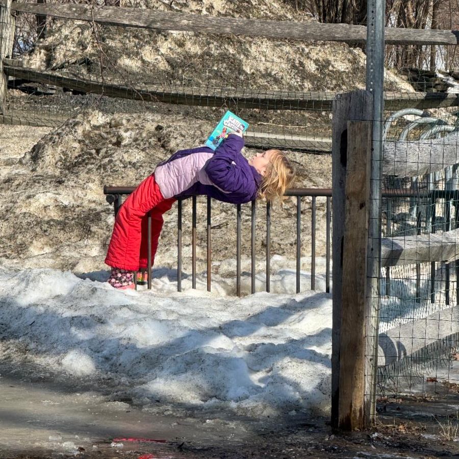 A student is leaning back on a bike rack, reading a book.