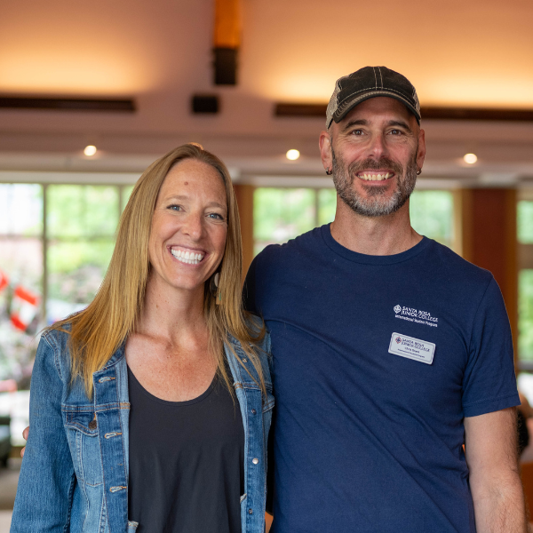Two SRJC counselors smile and stand together in a bright indoor space with international flags visible in the background.
