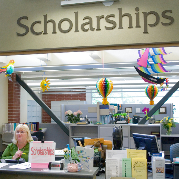 The SRJC Scholarships office with colorful hanging decorations and a staff member seated at the front desk.