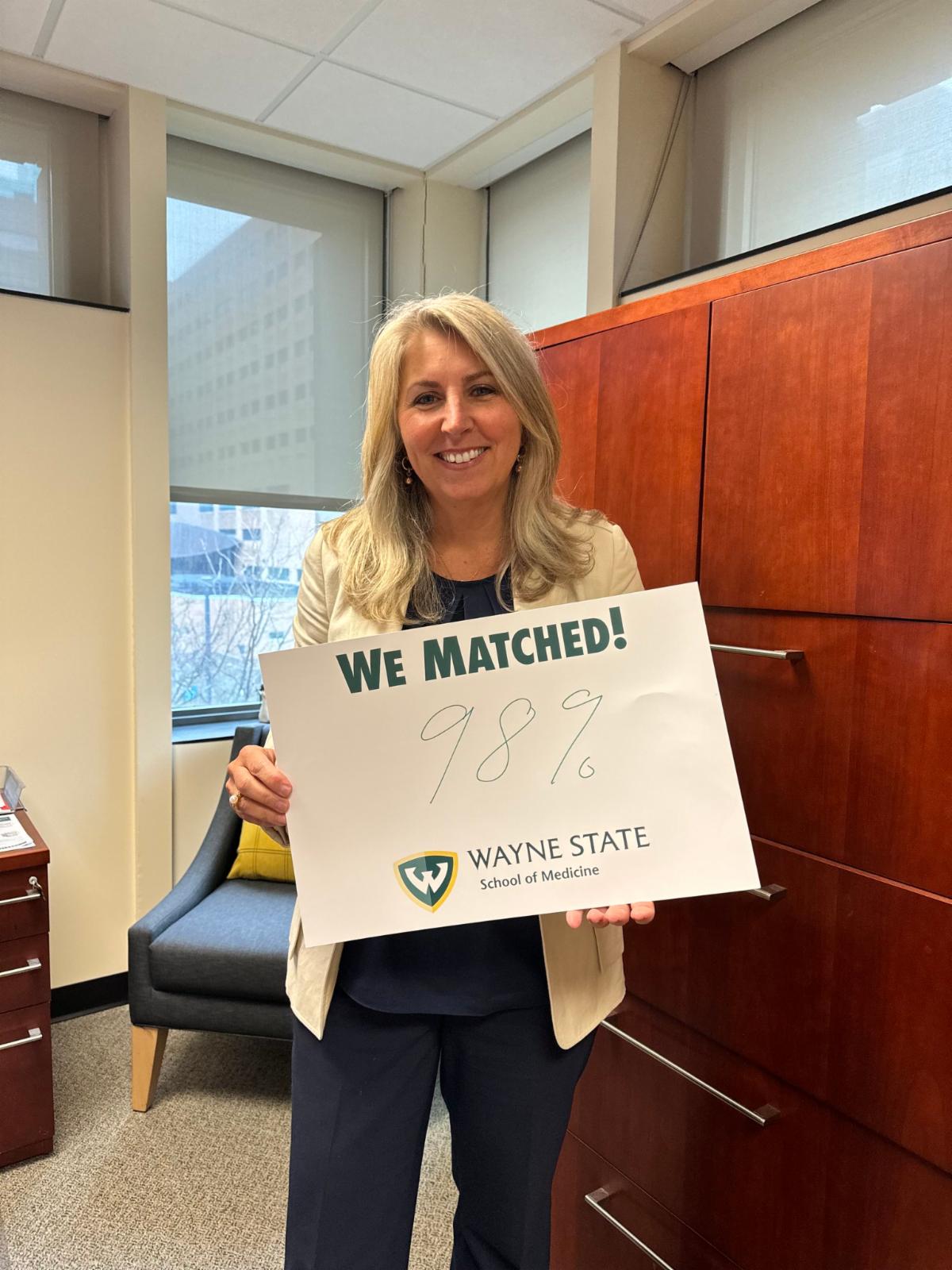 Dr. Margit Chadwell, a smiling blonde woman, holds a poster reading, "We matched! 98% Wayne State School of Medicine."