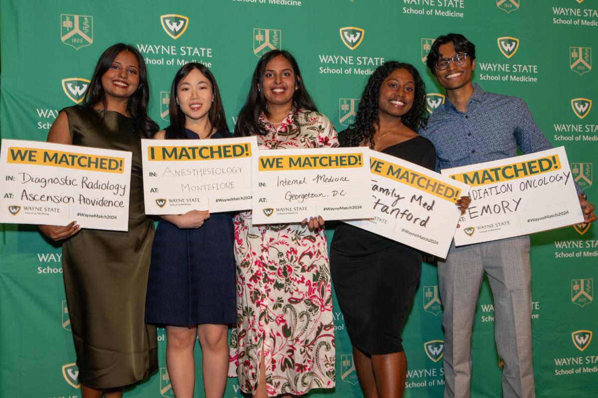 5 students (4 women and 1 man) in the class of 2024 hold "We Matched!" signs for a variety of residencies. They are smiling in front of a Wayne State University School of Medicine backdrop.