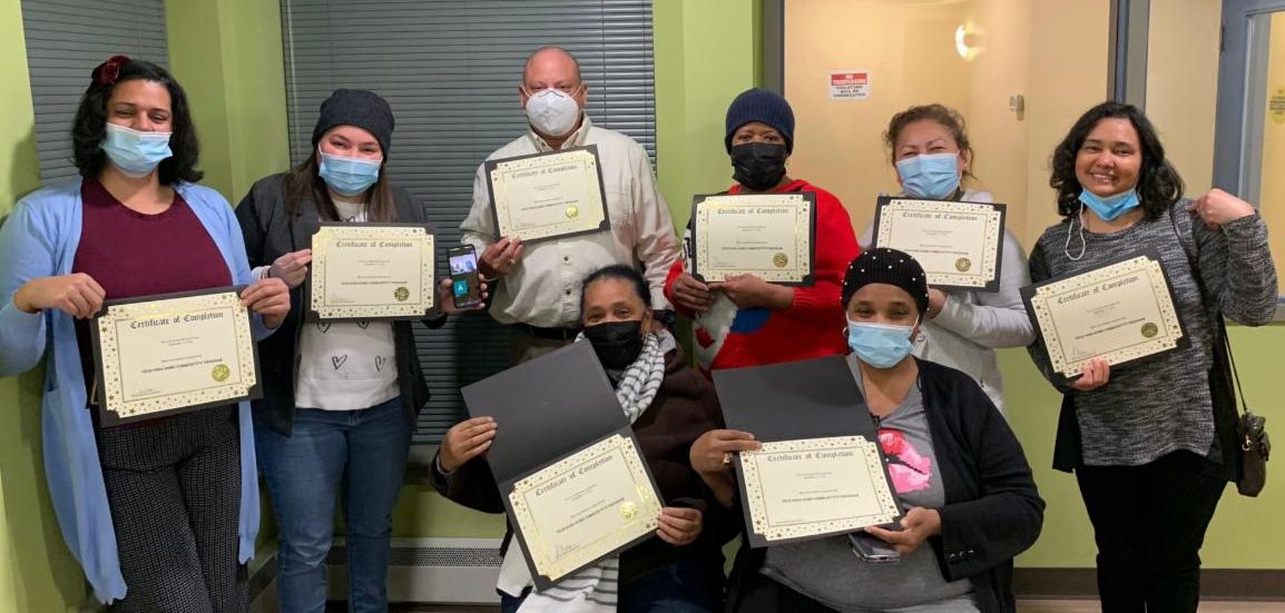 A group of adult learners face the camera holding their TGH certificates.