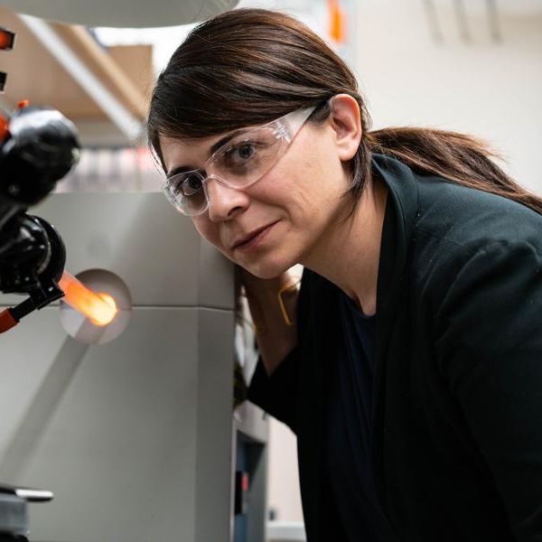 Desirée Plata in the lab wearing safety goggles and leaning over a machine.