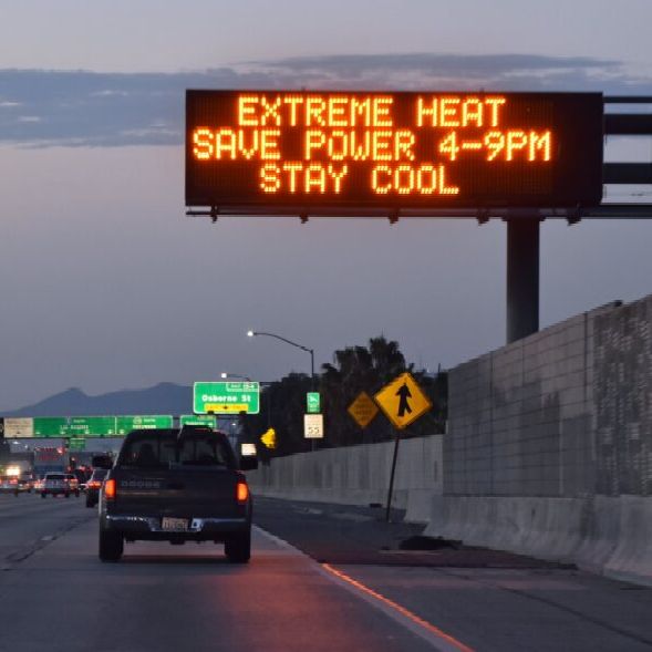 A car driving on a highway under a sign warning of extreme heat.
