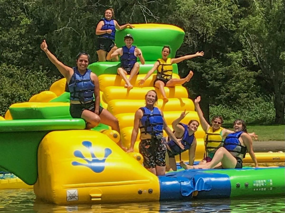 Adults in lifejackets play on inflatable water park