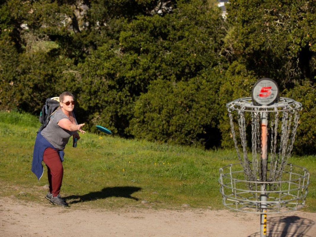 woman throws frisbee into a disc golf basket