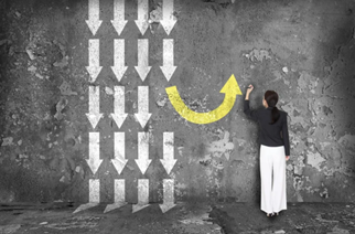 Conceptual image of a person drawing a yellow upward arrow on a concrete wall filled with white downward arrows, symbolizing changing direction or reversing a negative trend.