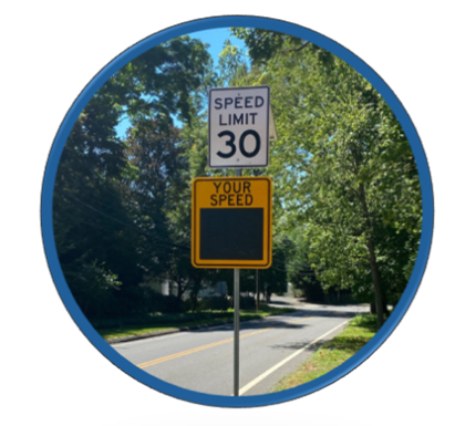 Speed limit sign showing 30 miles per hour with a digital Your Speed radar display below on a tree-lined road.