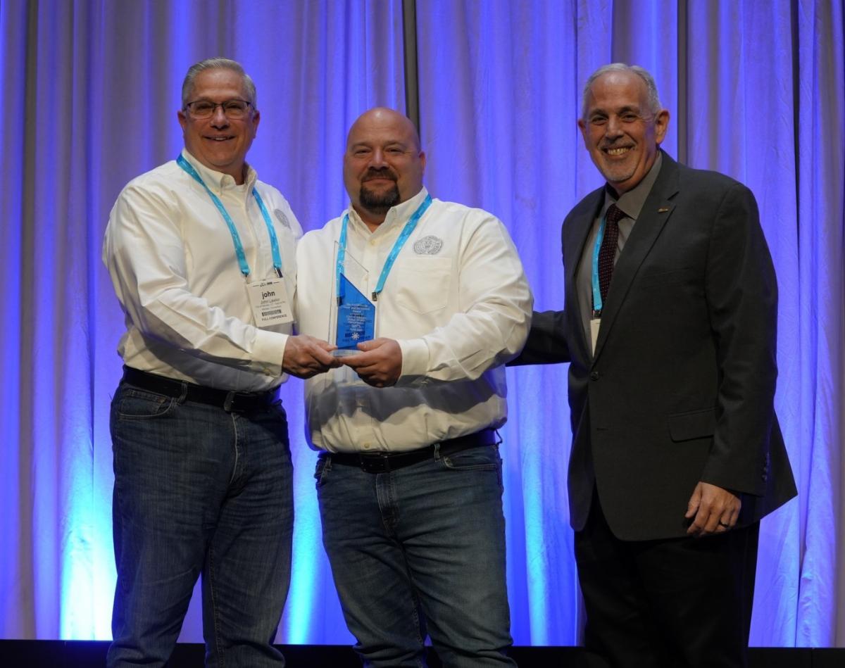 three men standing on a stage holding an award statue