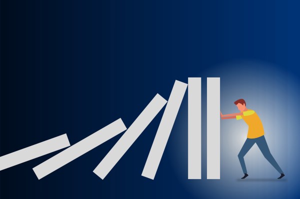 Illustration of a person in a yellow shirt and blue pants pushing against falling domino pieces to stop the chain reaction on a dark blue gradient background