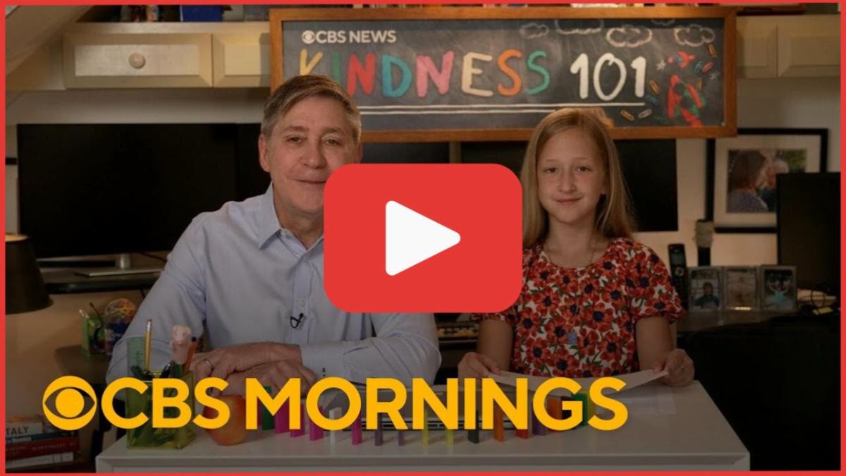 Video thumbnail showing an adult man and a young girl seated at a desk, smiling toward the camera, with a chalkboard behind them reading CBS News Kindness 101 and CBS Mornings text overlaid at the bottom.