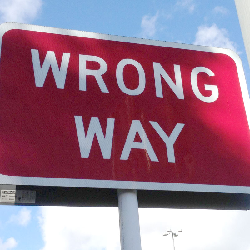 Red Wrong Way traffic sign with white lettering against a blue sky.