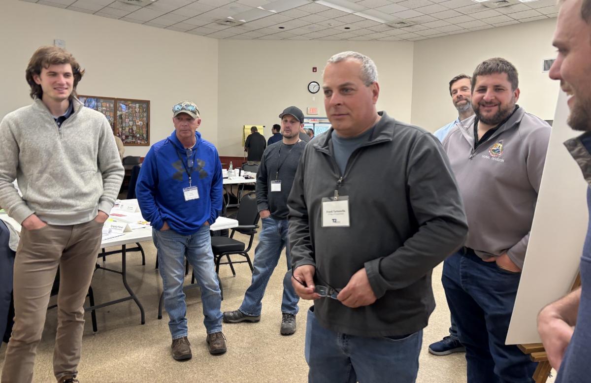 group of men standing and talking during a leadership training session appearing engaged and smiling in a classroom setting