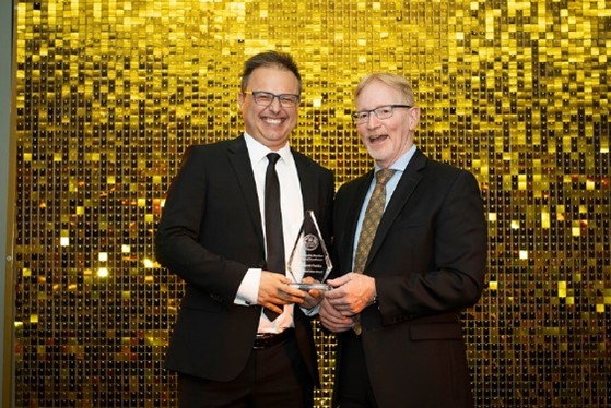 Dr David Ponka standing in front of a gold disco ball photo background with the Dean Dr. Bernard Jasmin