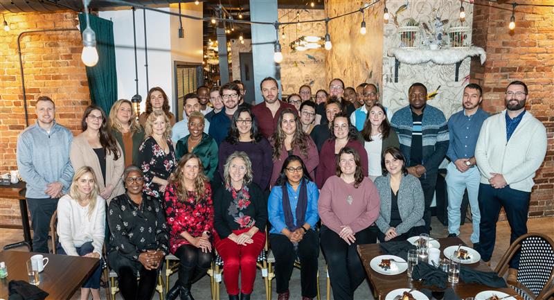 Department of Family Medicine Staff photo at their Staff Holiday Lunch on December 11 2024 in a restaurant with bright light and yellow brick walls