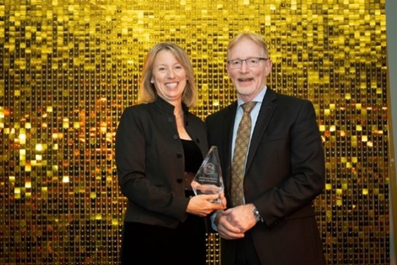 Dr Erika Tanner standing in front of a gold disco ball background holding her award with the Dean Dr Bernard Jasmin