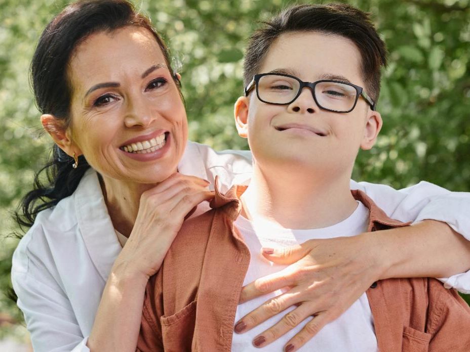 Mujer sonriendo y abrazando a un niño con síndrome de Down que también sonríe