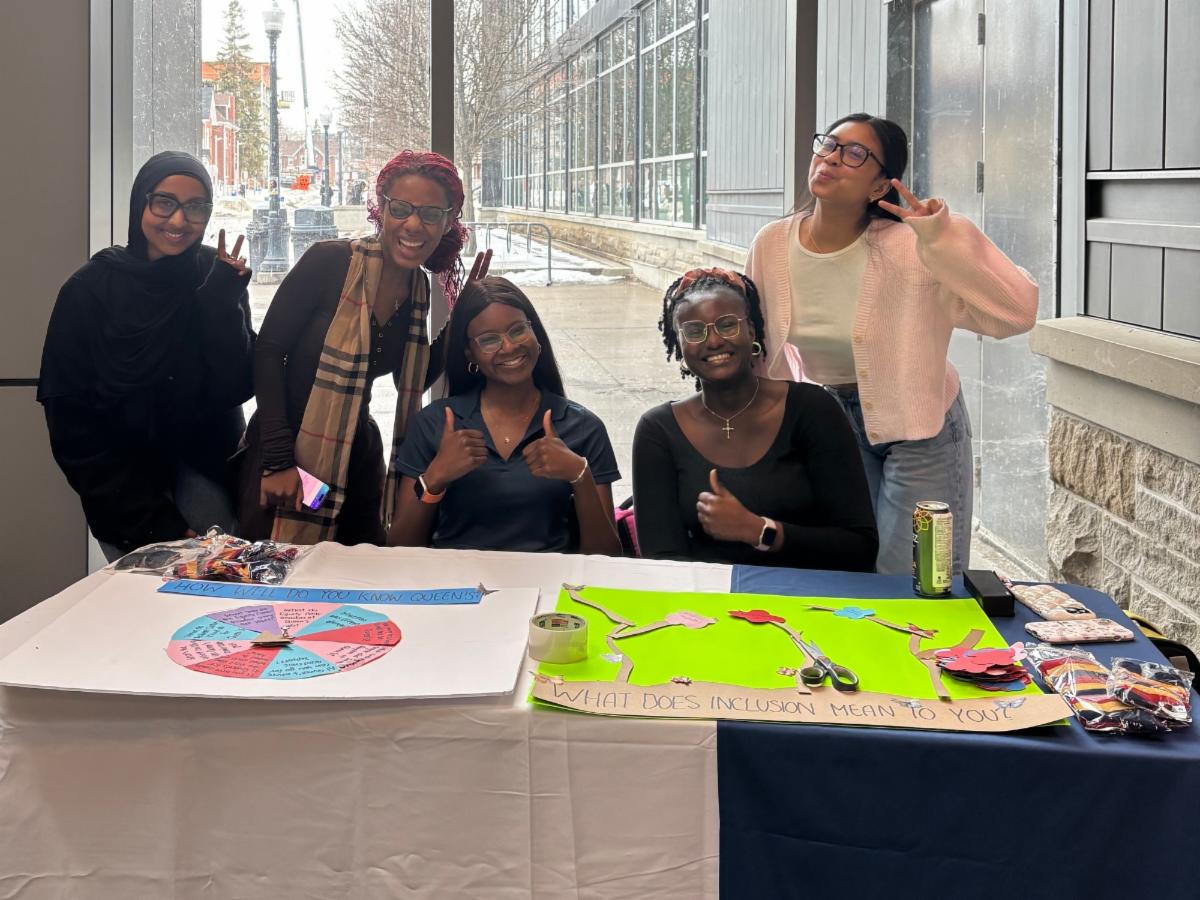 Five students behind a table, smiling, laughing, and holding peace signs.