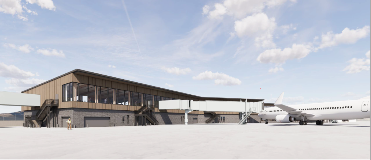 Modern airport terminal with large glass windows and jet bridges connected to a parked airplane on the tarmac under a mostly clear sky.