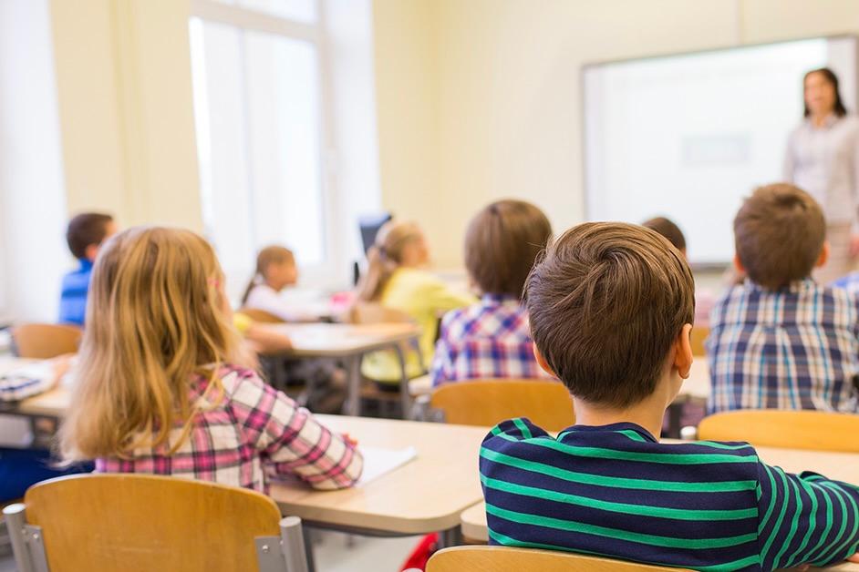 Classroom with young students sitting in desks facing a teacher at a blackboard.