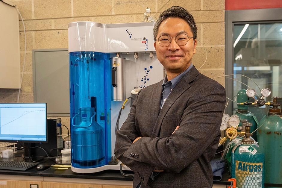 A man stands in a research laboratory with equipment in the background.