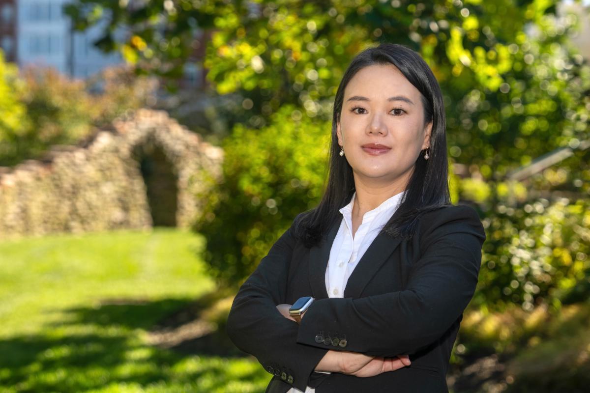 A person wearing a dark suit standing outside with trees in the background.