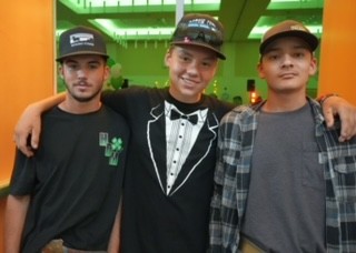 Three youth participants stand together with their arms around each other in a brightly lit indoor space, smiling and posing for a group photo.
