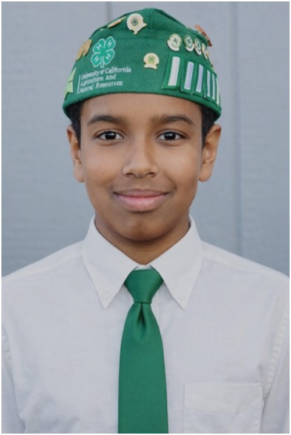 Photograph of Al-Yasa ‘ibn wearing a white dress shirt and green tie, with a 4-H hat with 4-H award stripes and pins.