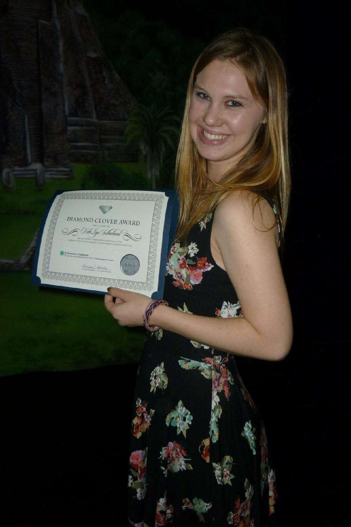 Kate Lyn smiling and holding her Diamond Clover certificate.   