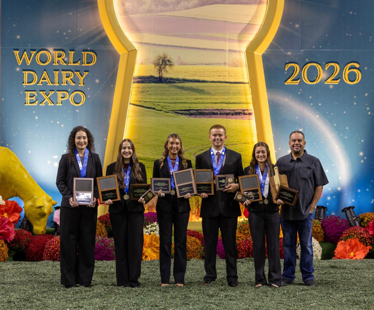 Photograph shows California 4-H Dairy Cattle Judging Team posing with plaques and medals at World Dairy Expo 2026. Colorful floral displays and a farm landscape backdrop frame the World Dairy Expo 2026 awards recognition ceremony.