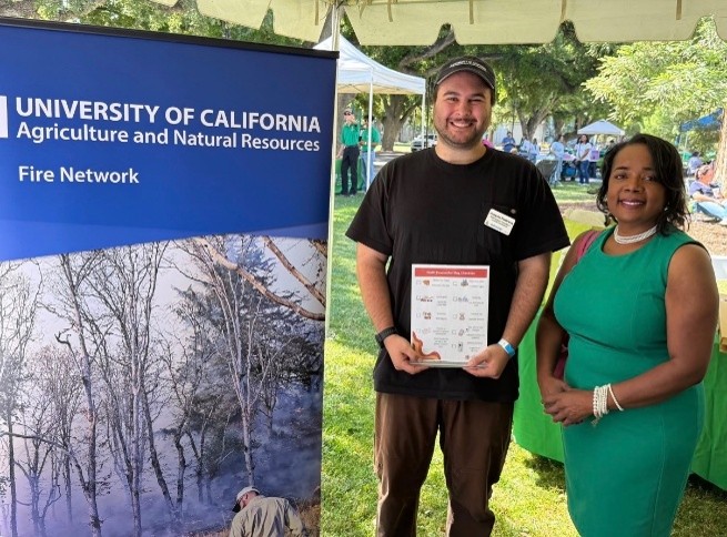 Dr. Holmes and Joaquin Pastrana of UC ANR Fire Network stand together in front of a Fire Network banner at State Field Day.